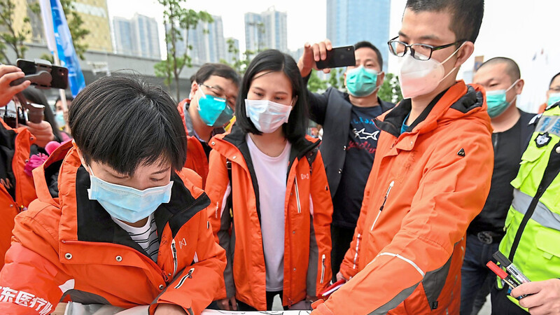 Helfer verlassen die Region Hubei im chinesischen Wuhan am Dienstag wieder. Zum Abschied unterschreiben sie aber noch auf einem Schutzanzug.