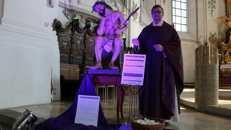 Pfarrvikar Markus Meier neben der illuminierten Christusfigur. Auf dem violetten Tuch davor kann jeder einen der weißen Steine, verbunden mit einem Anliegen, niederlegen.