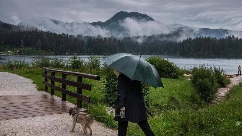 Eine Frau geht bei Regen mit ihrem Hund am Hintersee in Ramsau Bei Berchtesgaden spazieren.