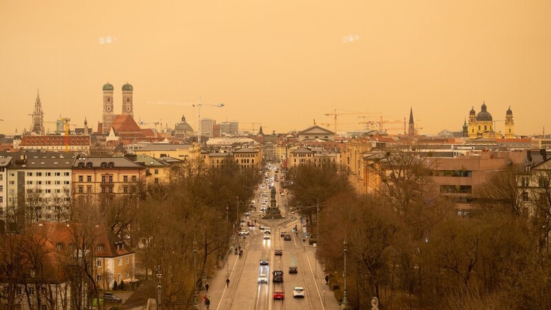 Über der Münchner Innenstadt zieht schlechtes Wetter mit Sahara-Staub auf, das den Himmel gelb/orange färbt.