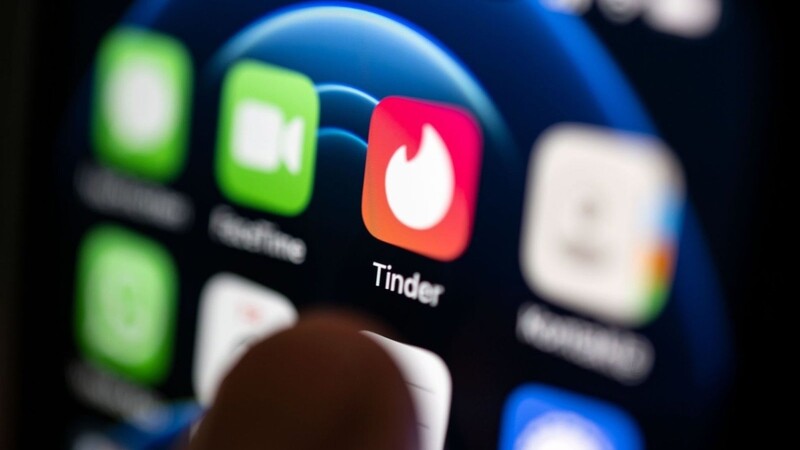 Ein Finger bedient ein Smartphone auf dem unter anderen die App von Tinder installiert ist.