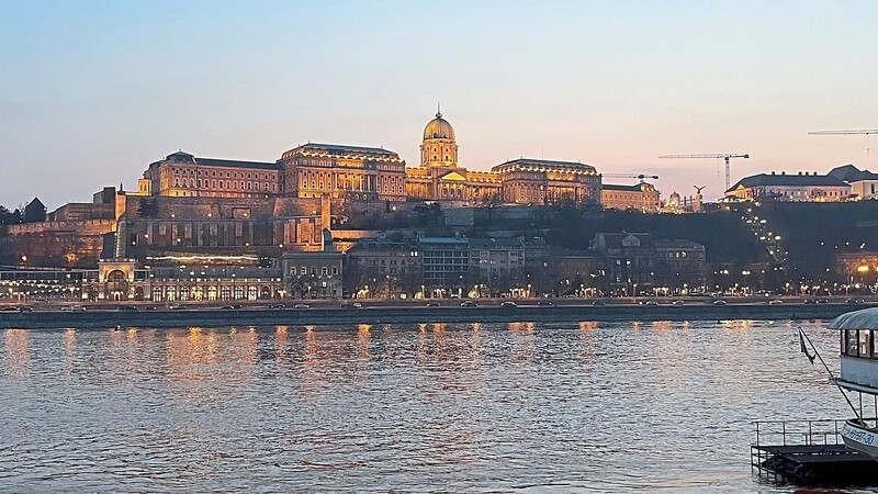 In den Abendstunden spiegeln sich die Lichter des Budapester Burgpalastes im Wasser der Donau.