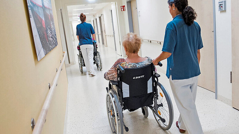Zwei Pflegerinnen schieben in einem Klinikum Patienten mit Rollstühlen durch einen Flur. Sie sind begehrte Fachkräfte, die immer rarer werden.
