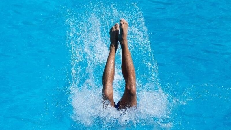 Ein junger Mann landet nach einem Sprung vom Drei-Meter-Brett im Wasser.