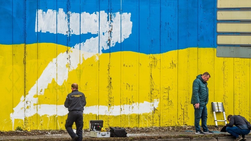 Ermittler suchen vor einer Wand, die in den Landesfarben der Ukraine angestrichen ist und auf die der Großbuchstabe Z gemalt wurde, nach Hinweisen. In Russland wird der Buchstabe Z zum Beispiel auf Autos, Häuser oder Kleidung geklebt. Sie bringen ihre Unterstützung für die russischen Streitkräfte in der Ukraine zum Ausdruck.