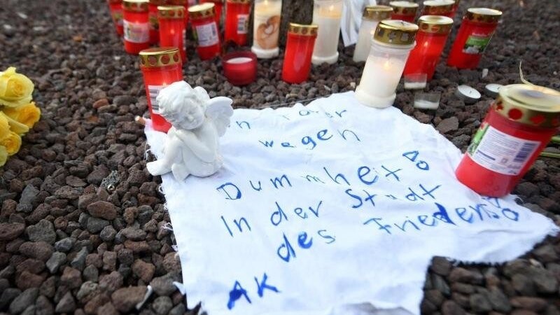 Am Königsplatz liegt eine Engelsfigur auf einem Stück Stoff, auf dem steht "Ein Toter wegen Dummheit! In der Stadt des Friedens!".