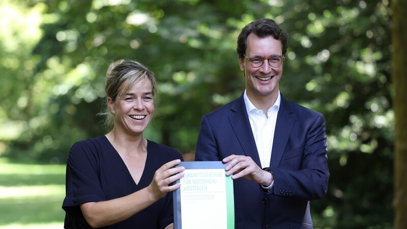 NRW-Ministerpräsident Hendrik Wüst (CDU) und Mona Neubaur, Vorsitzende der Grünen halten den schwarz-grün umrandeten Koalitionsvertrag in die Kamera.