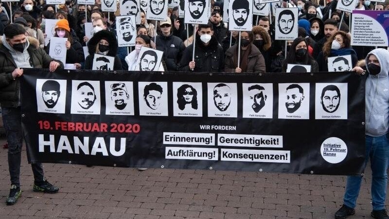 Mit Plakaten und Bildern der Ermordeten erinnern Teilnehmer einer Gedenkveranstaltung auf dem Marktplatz von Hanau an die Opfer der Anschläge von Hanau.