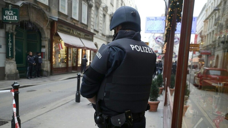Ein Polizist steht am Tatort hinter einem Absperrband. Nach Schüssen in der Wiener City ist nach Angaben der Einsatzkräfte ein Menschen gestorben, ein weiteres Opfer wurde schwer verletzt.