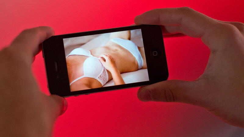 Ein junger Mann hält am 31.10.2013 in Hannover (Niedersachsen) ein Smartphone, auf dem ein erotisches Foto einer jungen erwachsenen Frau zu sehen ist.