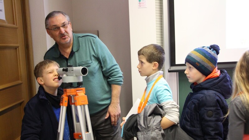 Vermessungsingenieur Werner Müller gibt mithilfe eines Vermessungsgeräts den Jungen und Mädchen einen Einblick in seine tägliche Arbeit.