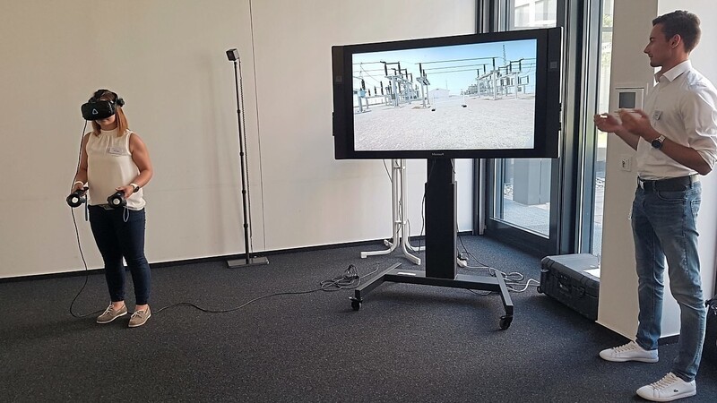 Bayernwerk-Mitarbeiter Stefan Keck erklärte, wie Augmented Reality bei der Wartung von Umspannwerken eingesetzt werden kann. Seine Kollegin streift mit einer VR-Brille virtuell durch ein Werk.