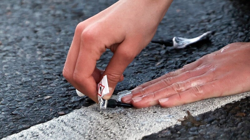 Ein Aktivist klebt seine Hand mit Sekundenkleber auf der Straße fest.