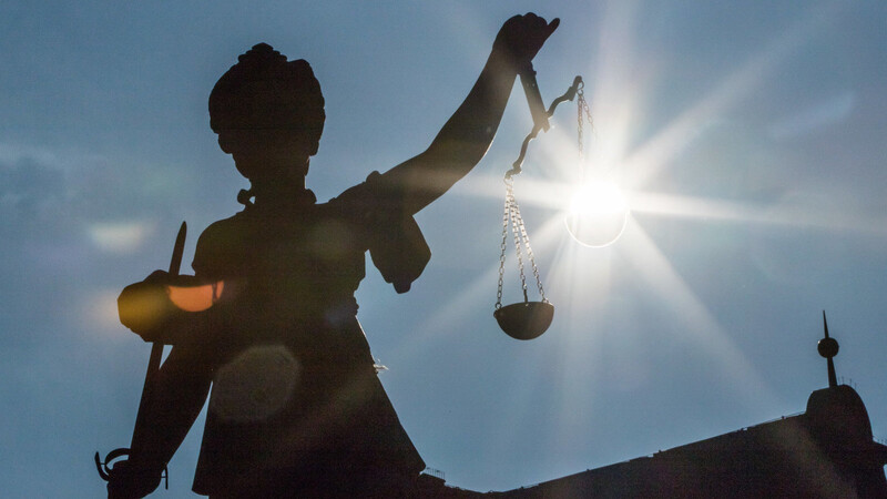 Die Morgensonne scheint auf eine Justitia-Statue vor einem Gerichtsgebäude.