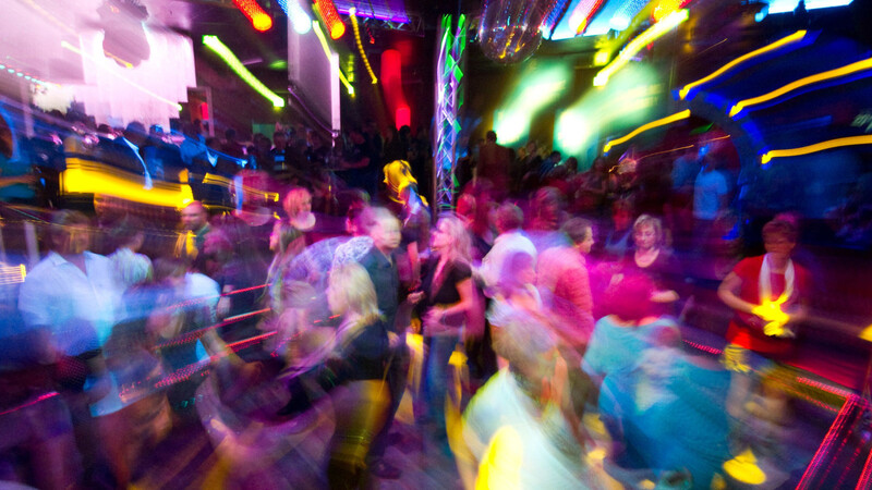 Partygäste tanzen in einer Diskothek. Wer noch nicht volljährig ist, muss die Gaststätte bis Mitternacht verlassen, außer ein Sorgeberechtigter begleitet ihn.