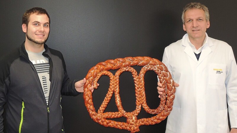 Bäcker Silvano Rödl ist der 200. Mitarbeiter der Bäckerei Mareis und wurde von Firmenchef Anton Mareis an seinem ersten Arbeitstag mit einer Riesenbreze im Unternehmen begrüßt.