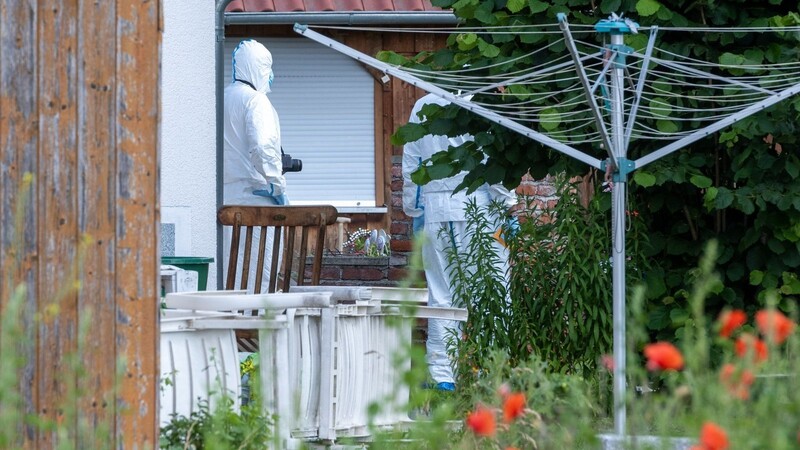 Polizeibeamte der Spurensicherung stehen im Garten des Hauses auf dessen Terrasse sich die Bluttat ereignete.