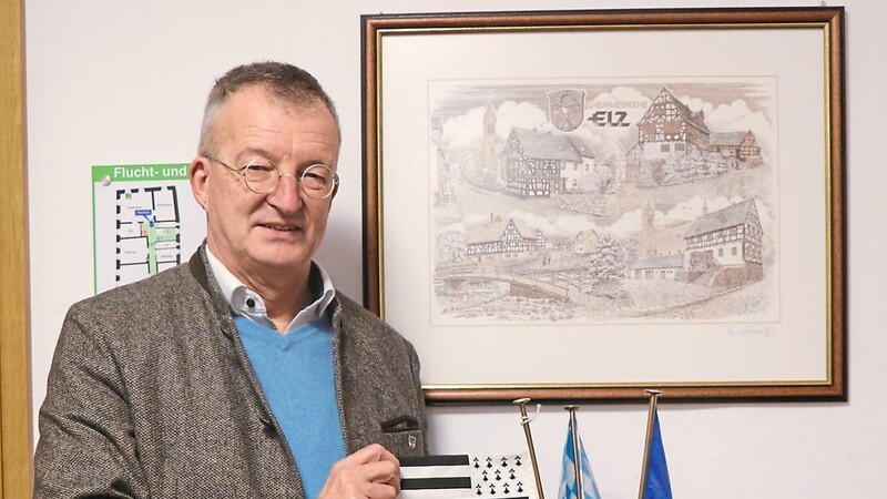 Bürgermeister Markus Ackermann vor einem Bild von Elz und mit Flaggen von der Bretagne (Combourg), Bayern (Marktoberdorf) und Tschechien (Klenči pod Čerchovem), die im Rathaus an die Partnerstädte Waldmünchens erinnern.