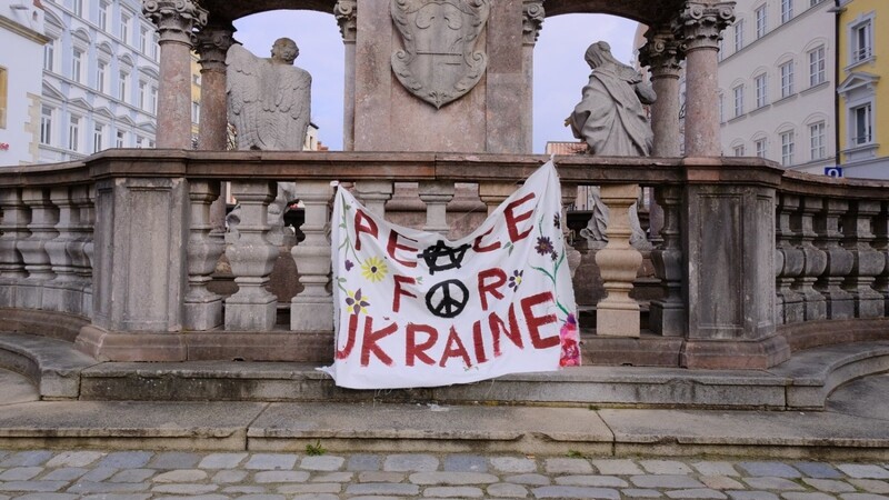 "Peace for Ukraine" steht auf einem weißen Stück Stoff, das an der Dreifaltigkeitssäule hängt. Seit Tagen wütet in der Ukraine ein Krieg, der Tausende Menschen zur Flucht bewegt.