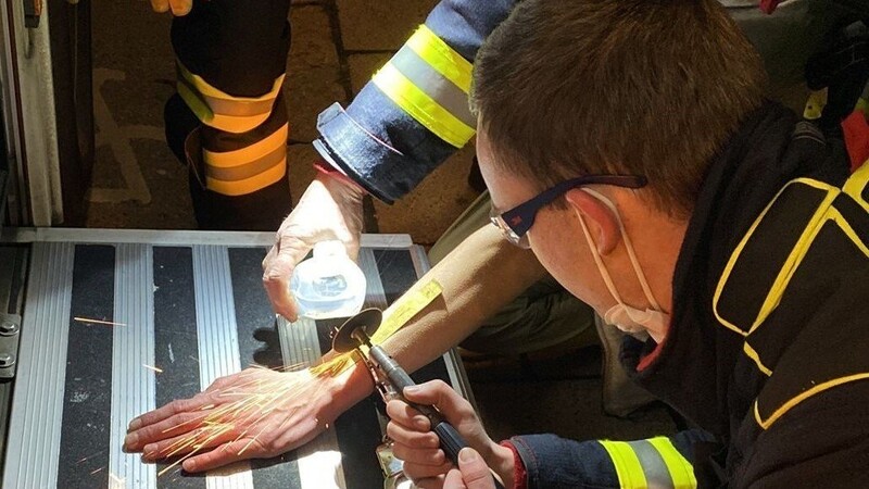 Ein Mann (Gesicht verdeckt) wird in München von der Feuerwehr und der Polizei mit einer Flex von einer Handschelle befreit.
