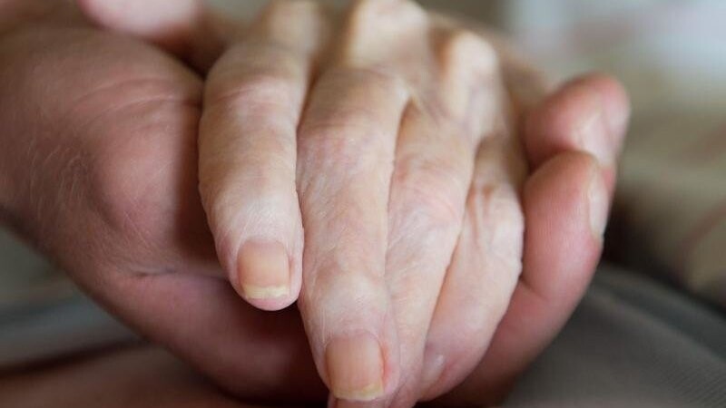 Ein Altenpfleger hält die Hand einer pflegebedürftigen Frau.