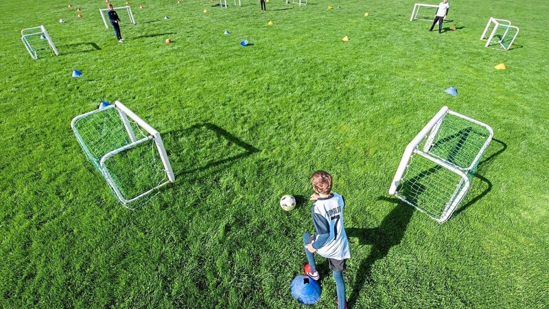 Fußballer der Altersklasse U-10 trainieren auf einem Spielfeld in großen Abständen.