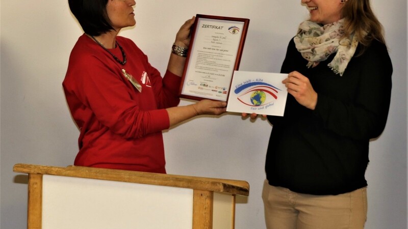 Kindergartenleiterin Elfriede Hartl (li.) nimmt aus den Händen von Caren Rehm vom Eine Welt Netzwerk Bayern das Zertifikat entgegen.