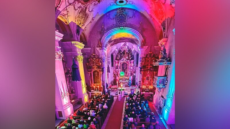 Die in buntes Licht getauchte Pfarrkirche während des modernen Abendgebetes im Scheinwerferlicht (MAISL)
