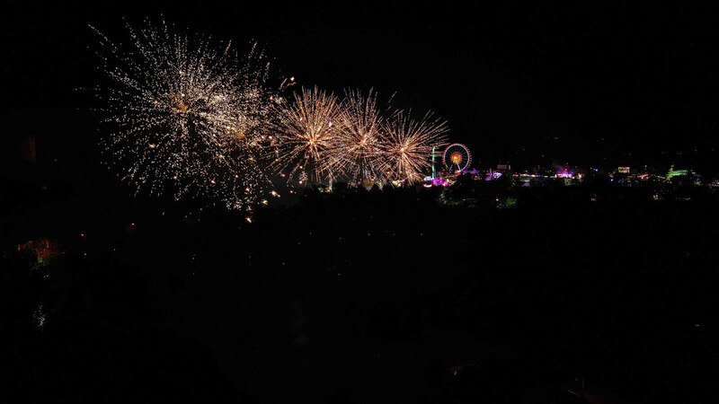 Im Vordergrund erhellt das Niederfeuerwerk den Himmel, während im Hintergrund die Volksfest-Lichter leuchten.