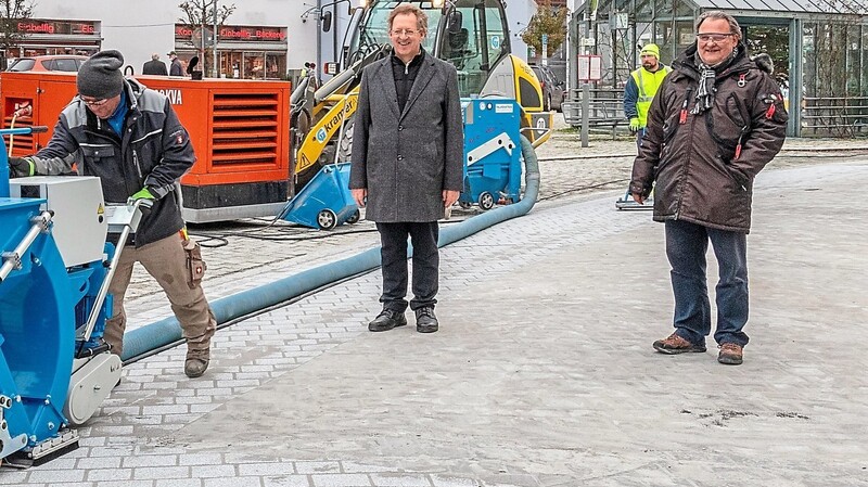 Ein Mitarbeiter strahlt den Straßenbelag neben Bürgermeister Christian Mayer (M.) und Bernd Burgetsmeier ab. Der Unterschied zu der früheren Art des Kopfsteinpflasters ist durch den Belag im Hintergrund sichtbar.