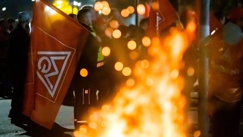 Streik an der Feuertonne: Ein Mann mit einer Fahne der IG Metall steht am Werk von Mercedes-Benz in Berlin-Marienfelde.