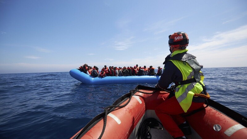 Migranten auf einem Schlauchboot werden von Mitarbeitern der Hilfsorganisation Sea-Eye vor der Küste Libyens gerettet. Die deutsche Hilfsorganisation Sea-Eye hat im Mittelmeer nach eigenen Angaben mehr als 60 Migranten, unter anderem auch Frauen, ein Kind und ein Baby, an Bord ihres Rettungsschiffes aufgenommen. Die Rettungsleitstellen in Italien und Malta hätten zuvor beim Angebot von Sea-Eye, bei der Suche nach Vermissten zu unterstützen, auf die Zuständigkeit der libyschen Küstenwache verwiesen. Nun warte die "Alan Kurdi", die unter deutscher Flagge fährt, auf die Zuweisung eines sicheren Hafens.
