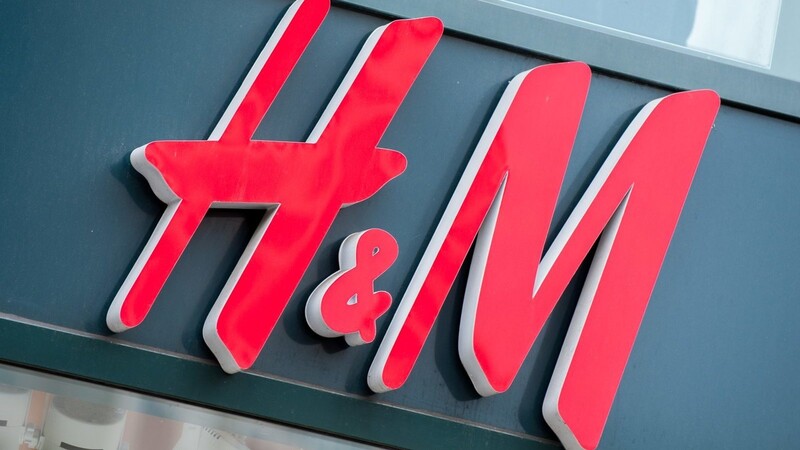 Das Logo der Bekleidungskette Hennes und Mauritz (H&M), hängt über dem Eingang einer Filiale.