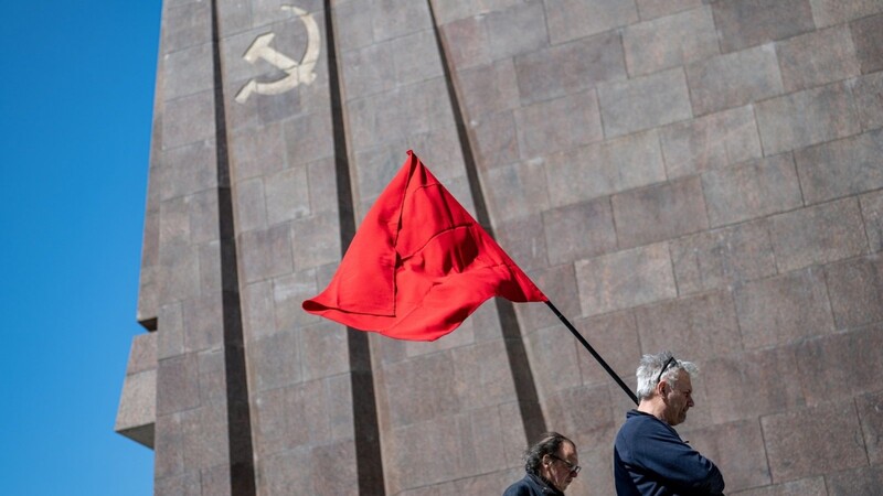 Ein Mann steht am Tag der Befreiung am 8. Mai vor dem Sowjetischen Ehrenmal im Treptower Park mit einer roten Fahne.