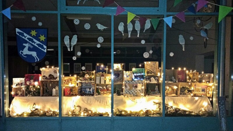 Mit Einbruch der Dunkelheit taucht das Weihnachtsschaufenster in der Aula der Montessori-Schule die Schaukästen in warmes Licht.