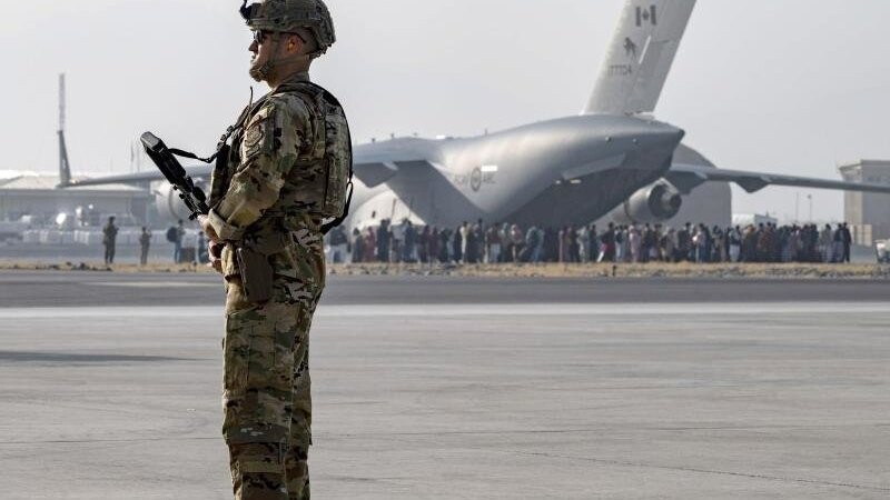 Ein Soldat der US-Luftwaffe steht auf dem Hamid Karzai International Airport in Kabul Wache. Vor den Toren des Flughafens stehen Tausende Menschen.