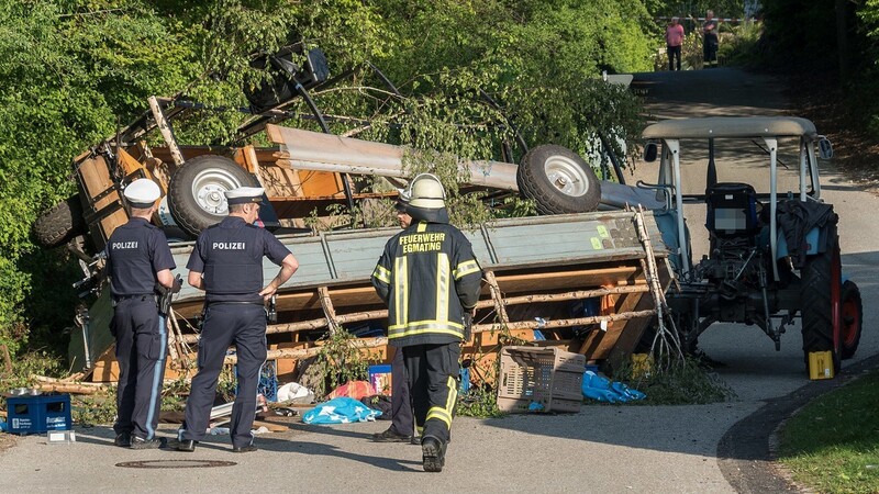 Polizisten und ein Feuerwehrmann stehen vor zwei umgestürzten Traktoranhängern. Der Traktor mit den Hängern voller feiernder Menschen war umgekippt. Zwei Menschen erlitten ersten Erkenntnissen zufolge schwere Kopfverletzungen, 15 weitere wurden leicht verletzt, wie das Polizeipräsidium Oberbayern Nord mitteilte.