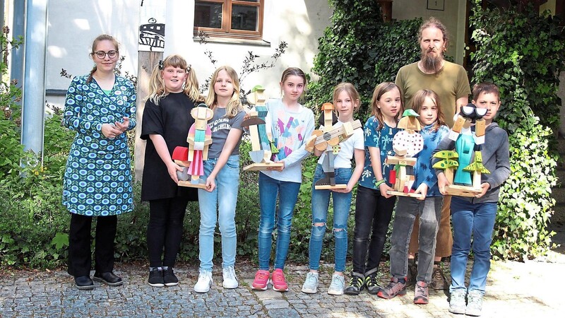 Julia Breu (links) und Andi Dünne zusammen mit einem Teil der jungen Künstler und einer Auswahl der Holzfiguren. Michaels (rechts) Förster wird auf die Stele beim Kunstbetrieb montiert.