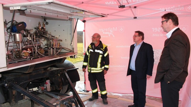 Örtlicher Einsatzleiter Martin Angermaier (v. l.) zeigt Staatssekretär Gerhard Eck und Landrat Martin Bayerstorfer einen Sauerstofftank.