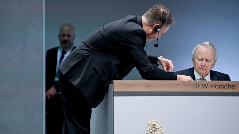 Aufsichtsratsvorsitzender Wolfgang Porsche (r.) auf dem Podium, an dem man einen Abdruck nach einem Tortenwurf sieht.
