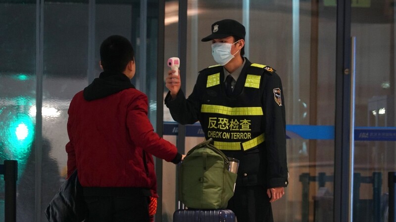 Ein Mitarbeiter des Flughafen Wuhan Tianhe International Airport trägt Mundschutz und misst bei einem Reisenden Temperatur. Dies gilt als Schutzmaßnahme gegen die Verbreitung des Corona-Virus.