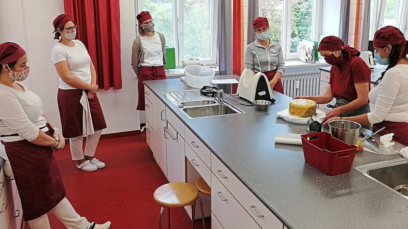 Praxis-Unterricht: Lehrkraft Margarete Renner zeigt den Studierenden die richtige Arbeitstechnik zum Dekorieren eines Tortenrands.  Foto: AELF