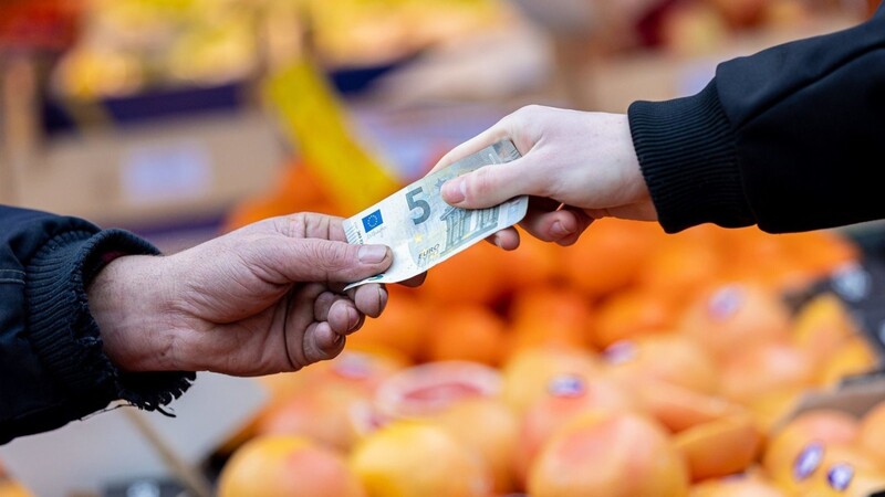 Ein Kunde bezahlt seinen Einkauf an einem Stand auf einem Wochenmarkt mit einem Fünf-Euro-Schein (gestellte Szene). Die Lebensmittelpreise steigen deutlich. Nun gibt es in der EU neue rechtliche Möglichkeiten zur Senkung der Mehrwertsteuer.