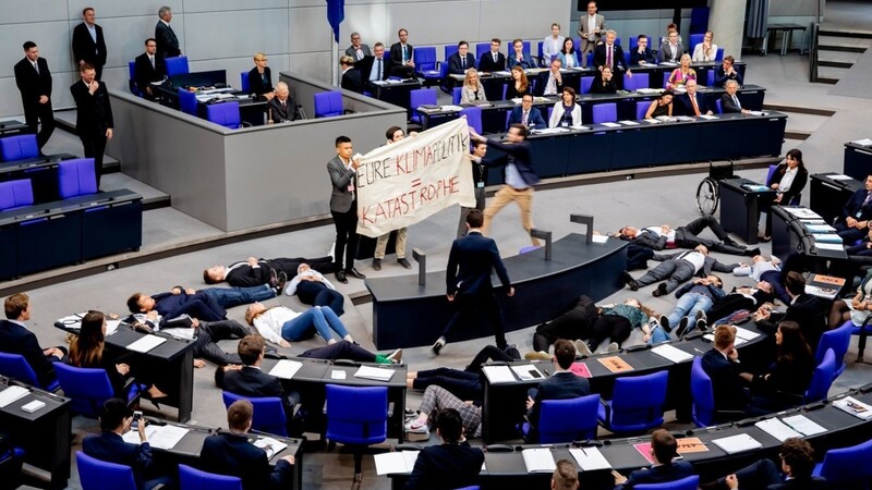 Teilnehmer einer Protestaktion für Klimagerechtigkeit von Fridays For Future halten im Plenarsaal des Bundestages ein Banner hoch, als ein junger Mann herbeieilt, um das Banner zu entfernen und den Protest zu stören. Beim Planspiel "Jugend und Parlament" schlüpfen Jugendliche in die Rolle von Bundestagsabgeordneten.