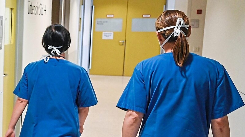Zwei Pflegerinnen gehen in einem Krankenhaus an dem Schriftzug "Intensiv" vorbei.