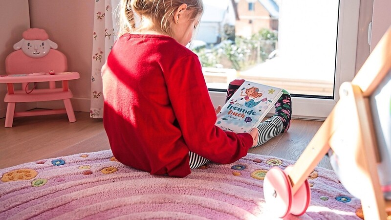 So isoliert sieht es nicht nur im Frühjahr 2020 in vielen Kinderzimmern aus: Ein kleines Mädchen blättert allein in einem Kinderbuch.