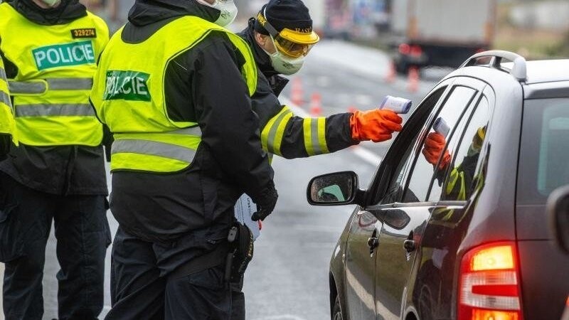 Ein Feuerwehrmann aus Tschechien misst neben Polizisten die Temperatur von einem Einreisenden an der Grenze.