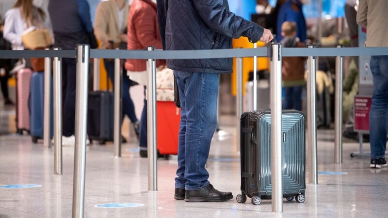 Reisende stehen am Flughafen München mit ihren Koffern an einem Check-In Schalter.