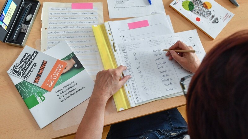 Eine Lehrerin kontrolliert Übungsblätter für Analphabeten. Millionen Menschen gehen in Deutschland mit Lese- und Schreibschwäche durch den Alltag.