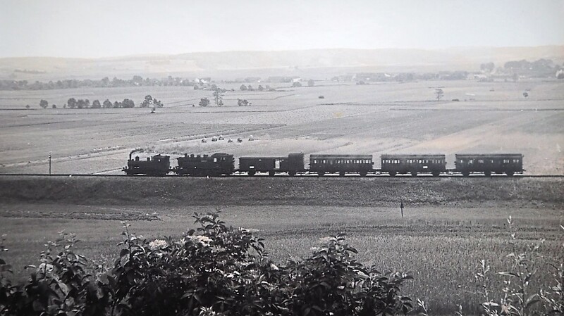 Landschaftsaufnahme eines Zugs, der 1957 an Poxau vorbei in Richtung Pilsting fährt. Bemerkenswert ist, dass hier zwei Loks vorgespannt sind.